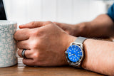 Aquacy Mesh Bracelet Watch Blue And Black On Wrist Holding Cup